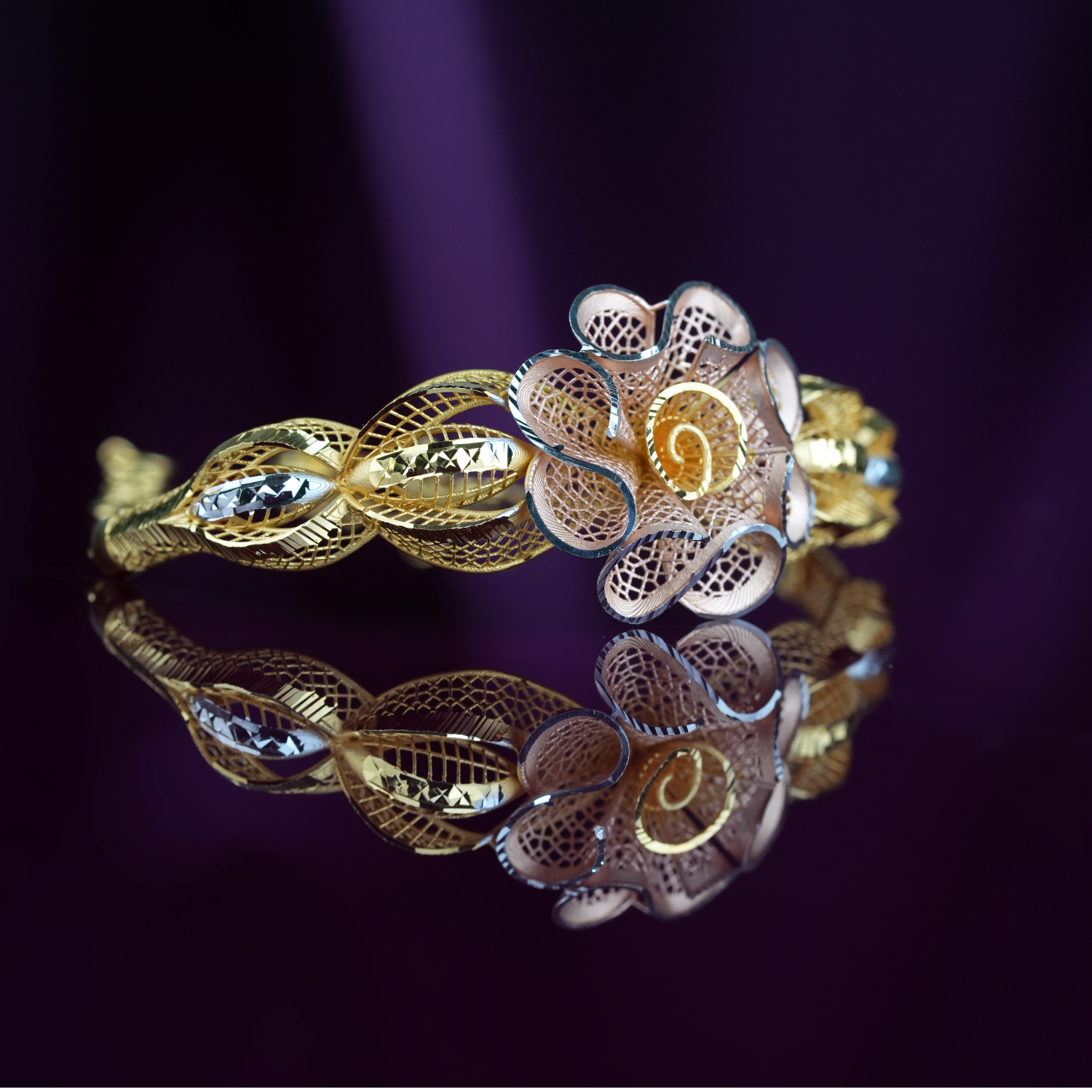 Daisy Vale 18kt gold bracelet by Taqwa Jewellers with a curled-petal flower centre and woven eye-shaped links.
