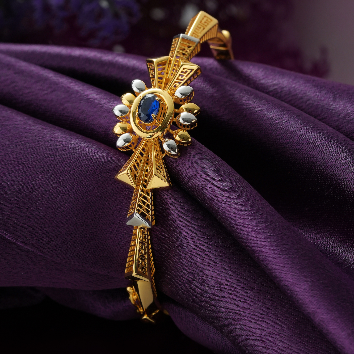 22KT gold bracelet with an oval blue centre stone, ring of yellow and rhodium petals and a key-pattern cut-out band.