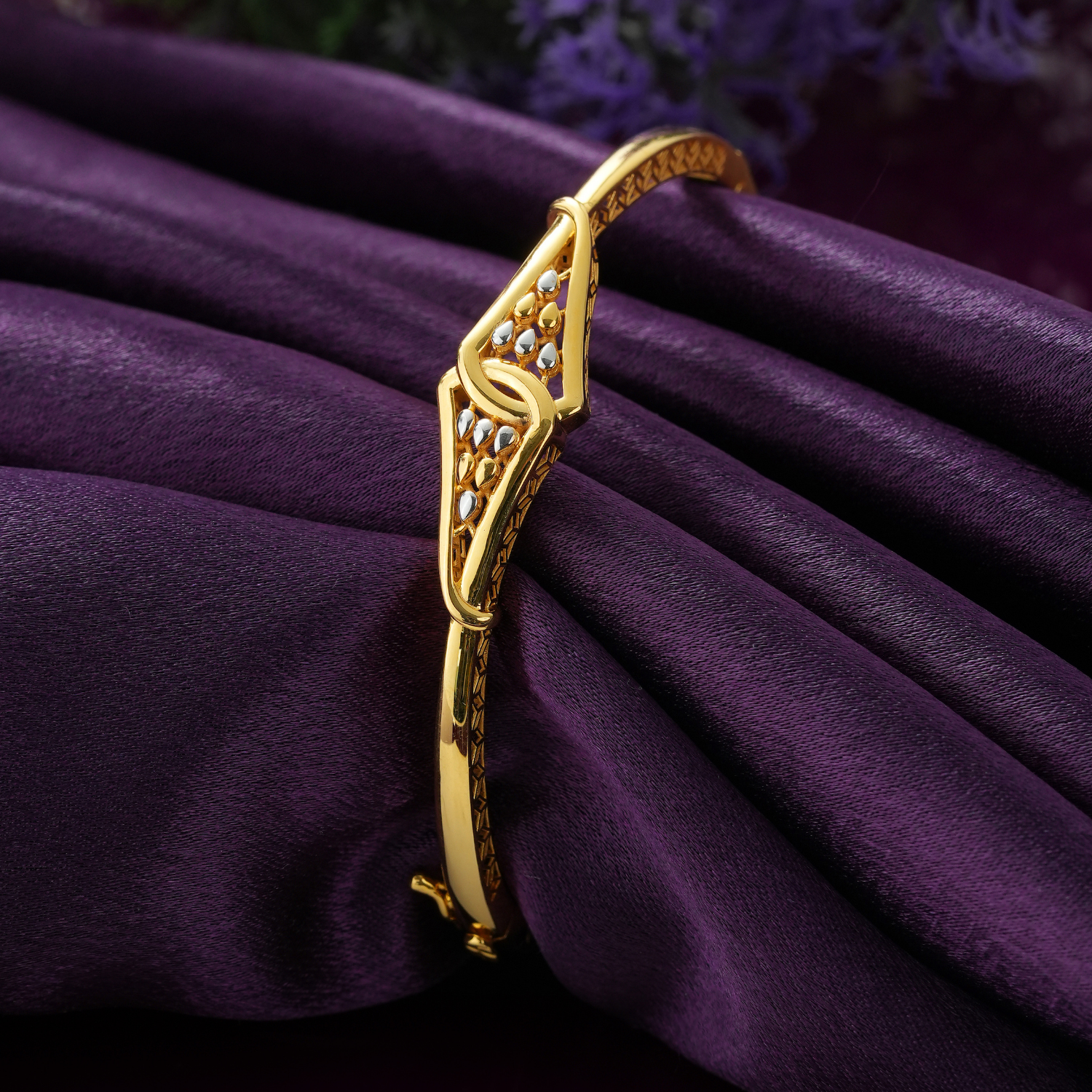 18KT gold bracelet with a diamond-shaped looped front, gold and rhodium drop shapes and a slim glossy band.