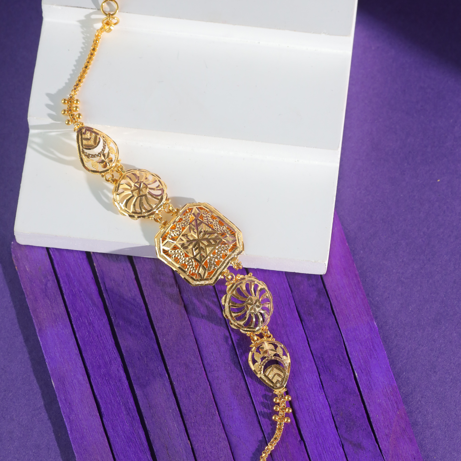 18KT yellow gold bracelet with an eight-sided star-pattern panel, round spoke medallions and teardrop shapes on a chain.